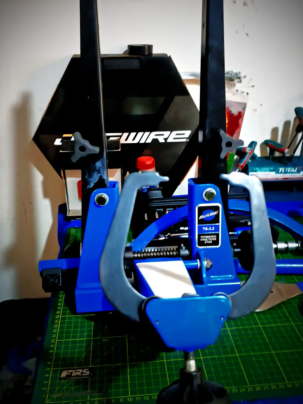 Centrador de ruedas Park Tool TS-2 sobre esterilla de corte en el banco de trabajo, con los brazos y las guías de medida en primer plano — BikeLab Studio · Carlos Eduardo Ravello Joo